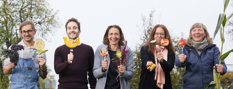 Mehrere Menschen stehen in einem Garten und halten Gabeln vor ihrem Körper. Auf den Gabeln ist unterschiedliches Gemüse aufgesteckt. Die Menschen lächeln. Danke für Ihre Unterstützung für ein vielfaltsförderndes Saatgutrecht!